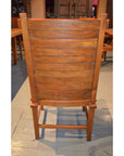 Brown teak armless chair with curved slats, rear view, on a tiled floor.