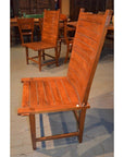Brown wooden Arts & Crafts style armless chair with tall curved slatted back among other chairs and tables.