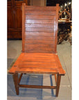 Brown teak armless chair with horizontal slats, Arts & Crafts style, on a gray indoor floor.