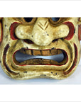 Close-up of a Balinese dancing mask with red accents, large nose, and open mouth, made of painted material.