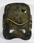 Brown hand-carved wood mask with two eye holes, rectangular mouth, and a string across the face, close-up.