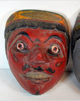Close-up of a painted wooden Balinese mask with red face, wide eyes, mustache, and yellow-green headband.