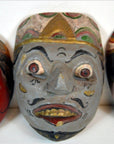 Colorful wood Balinese dancing mask close-up with bulging eyes, pointed nose, mustache, patterned headdress.