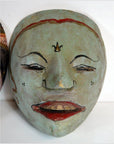 Close-up of pale green Balinese dancing mask with red lips and black and red facial features, carved wood.