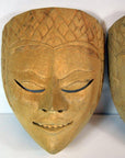 Close-up of brown carved wood Balinese dancing mask with closed eyes, subtle smile, ornate forehead patterns.