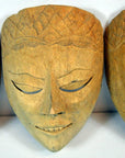 Light wood Balinese dancing mask with delicate carving, closed eyes, and a subtle smile on a light background.