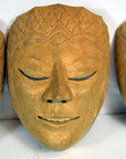Close-up of a carved wood Balinese dancing mask with closed eyes, delicate etched patterns, and a serene expression.