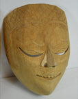 Close-up of a Balinese dancing mask with closed eyes, gentle smile, and detailed forehead patterns, wood material.
