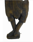 Brown wooden statue of Balinese temple dancer with crossed legs in shorts, displayed as wall decor.