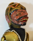 Close-up of hand-carved Balinese puppet with painted face, gold headdress, prominent teeth, black and gold costume.