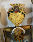 Close-up of hand-carved wooden Balinese puppet with painted face, gold arms, ornate headpiece, embroidered clothing.