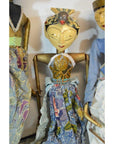 Colorful wooden Balinese puppets with gold headdress, painted faces, and batik clothing, standing indoors.
