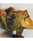 Close-up of a red and gold hand-carved wooden Balinese puppet head with intricate carvings, indoors.