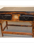 Black lacquered and bamboo desk with dark top and two open drawers with metal handles, indoor setting.