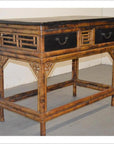 Black lacquered desk or console with black drawers and bamboo legs, placed on a gray floor against a white wall.