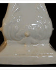 White porcelain candle holder with ornate raised details on pedestal base, close-up against black background.