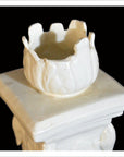 White porcelain candle holder with irregular rim on square base, close-up against a deep black background.
