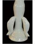 White Blanc de Chine porcelain candle holder with two dolphin figures, close-up on black background.