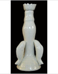 White porcelain candle holder with dolphin figures on a flared base, displayed against a black background.