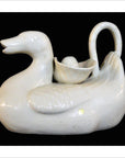 White porcelain duck-shaped teapot with shell cup and egg, close-up on black background.