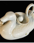 White porcelain duck-shaped pitcher with handle and bowl, set against a black background.