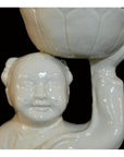 White porcelain monk figurine holding a bowl, Blanc de Chine style, close-up against solid black background.