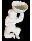 White porcelain monk figurine kneeling and holding a scalloped bowl, displayed against a black background.