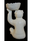 White porcelain monk figurine holding a scalloped bowl, rear view, Blanc de Chine style, black background.