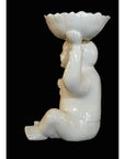 White porcelain monk figurine with scalloped bowl overhead, side view against black background.