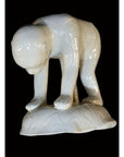 White porcelain monkey sculpture, Blanc de Chine, on hands and feet with head bowed, displayed on a small base.