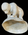White porcelain monkey holding open shell, Blanc de Chine style, close-up against black background.