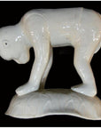 Close-up of white Blanc de Chine porcelain monkey, crouched on textured base against a black background.