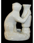 White porcelain monkey figurine hugging tall vase, close-up against dramatic black background.