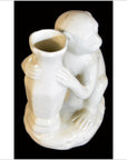 White porcelain monkey figurine holding tall angular vase on black background, close-up.