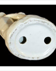 Close-up bottom view of white porcelain Blanc de Chine monkey with two circular holes on base, black background.