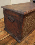 Brown carved Indonesian wood blanket chest on wooden floor.