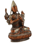 Brass deity statue in ornate robes and pointed hat, seated peacefully, brass details visible, close-up view.