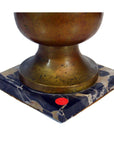 Close-up of brass lamp with shade on square marble base, small red dot sticker in corner.