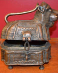 Close-up of brass animal-shaped monkey box with hinged lid slightly open, set against a solid red background.