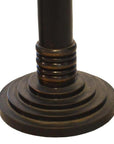 Close-up of bronze metal candle holders with dark, round, tiered bases and concentric rings, vertical pole design.