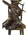 Bronze child doll sculpture smiling, sitting on chair with arms and legs extended, close-up view.