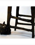 Bronze cat sculpture beside wooden chair legs and rungs, indoors.