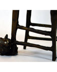 Bronze cat sculpture beside wooden chair legs and rungs, indoors.