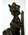 Bronze sculpture of abstract seated draped female figure in profile on plain background.