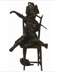 Bronze doll of a playful child sitting on chair with a cat in their lap and another cat beside the chair.