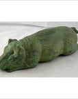 Green bronze pig sculpture with textured surface, reclining with outstretched legs, tabletop decor close-up.