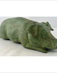 Bronze pig figurine lying down on a white surface, close-up, decorative tabletop object.