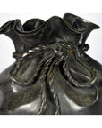 Close-up of a dark ceramic vase shaped like a tied bag, called the Bronze Pouch, on a tabletop.