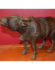 Close-up of a detailed bull sculpture made of metal on a wooden surface with a red wall background.