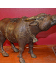 Bronze bull sculpture with detailed features on a wooden surface, set against a red wall.
